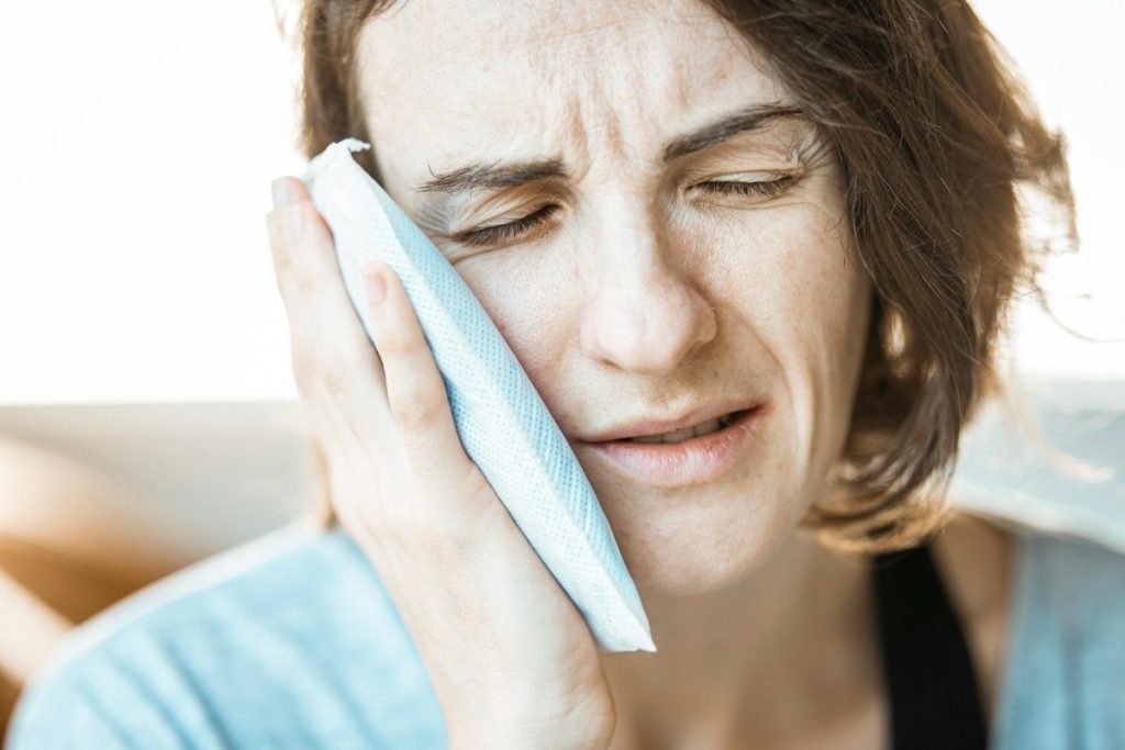 Woman holding a cold compress on her cheek to relieve toothache pain. Is My Tooth Infection an Emergency?